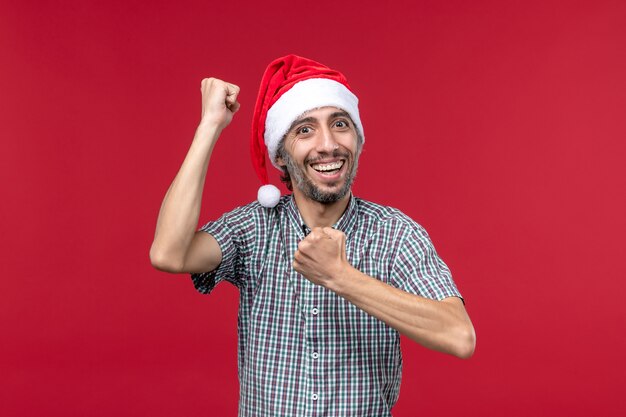 Vista frontal joven con expresión sonriente en la pared roja masculina de vacaciones de año nuevo rojo