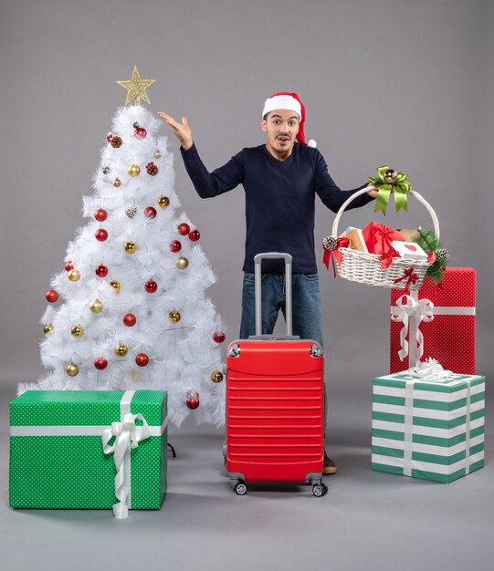 Vista frontal joven con gorro de Papá Noel con canasta de regalo en gris aislado