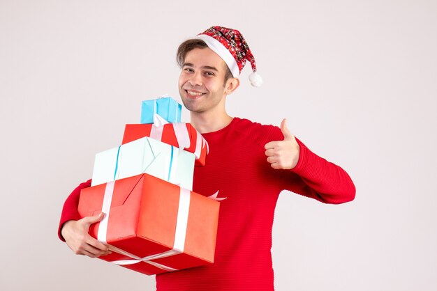 Vista frontal joven con gorro de Papá Noel haciendo pulgar arriba signo sobre fondo blanco.