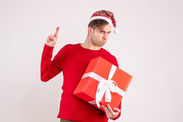 Vista frontal joven con gorro de Papá Noel haciendo signo de buena suerte de pie sobre fondo blanco.