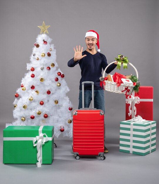 Vista frontal joven con gorro de Papá Noel mostrando cinco en gris aislado