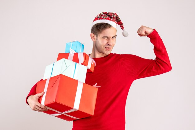 Vista frontal joven con gorro de Papá Noel mostrando su brazo mucsle sobre fondo blanco.