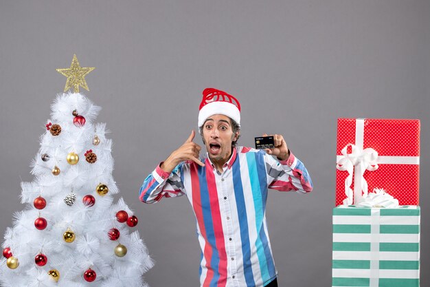 Vista frontal joven con gorro de Papá Noel que muestra la señal de teléfono llámame