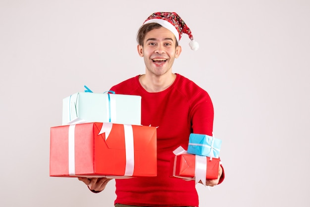 Vista frontal joven con gorro de Papá Noel sosteniendo regalos sobre fondo blanco.