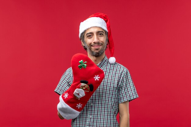 Vista frontal del joven con gorro rojo de Navidad en la pared roja