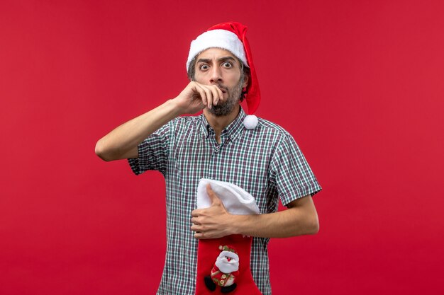 Vista frontal del joven con gran calcetín de Navidad en la pared roja