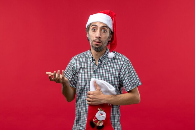 Vista frontal del joven con gran calcetín de Navidad en la pared roja