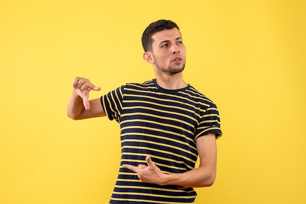 Vista frontal joven guapo en camiseta a rayas blanco y negro fondo amarillo aislado