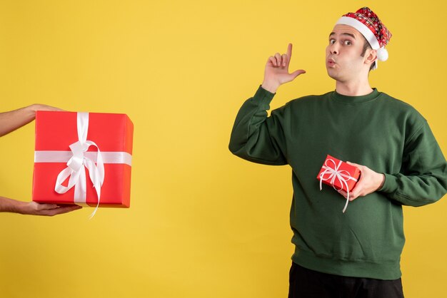 Vista frontal joven haciendo pistola de dedo firmar el regalo en mano femenina en amarillo