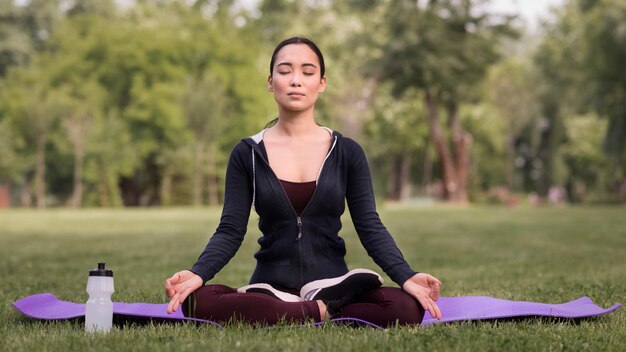 Vista frontal joven haciendo yoga al aire libre