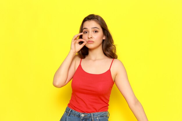 Una vista frontal joven hermosa en camisa roja y jeans azul cerrando la boca