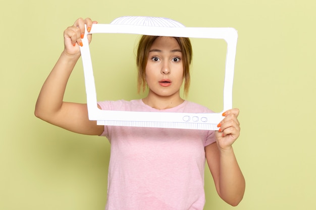 Foto gratuita una vista frontal joven hermosa en camiseta rosa posando con papel en forma de tv blanca en verde