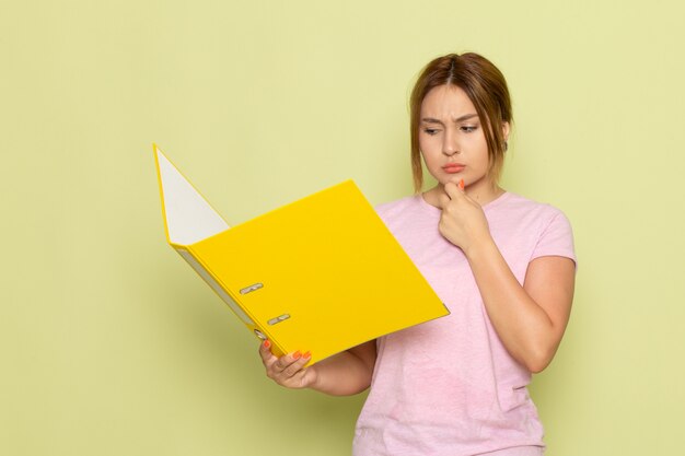 Una vista frontal joven hermosa en jeans azul camiseta rosa leyendo archivo amarillo con expresión de pensamiento en verde