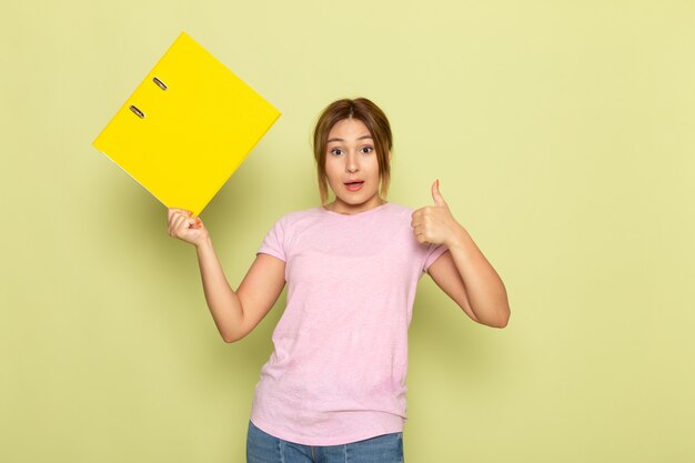 Una vista frontal joven hermosa en jeans azul camiseta rosa posando con archivo amarillo en verde