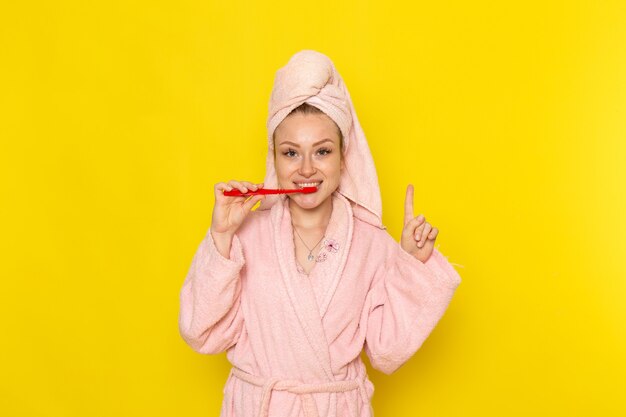 Una vista frontal joven hermosa mujer en bata de baño rosa limpiando sus dientes