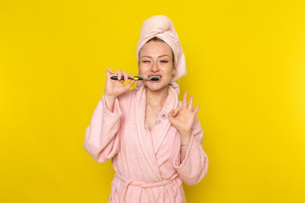 Una vista frontal joven hermosa mujer en bata de baño rosa limpiando sus dientes