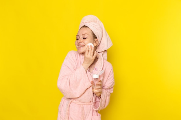 Una vista frontal joven hermosa mujer en bata de baño rosa limpiando todo el maquillaje con una sonrisa