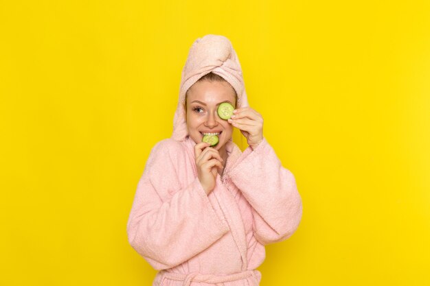 Vista frontal joven hermosa mujer en bata de baño rosa con rodajas de pepino