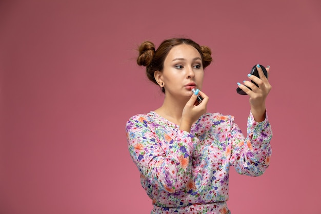 Vista frontal joven hermosa mujer en camisa de flor diseñada y jeans azul haciendo maquillaje en el fondo rosa