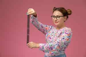 Foto gratuita vista frontal joven hermosa mujer en camisa de flor diseñada y jeans sosteniendo cinta de cine vieja en el fondo rosa