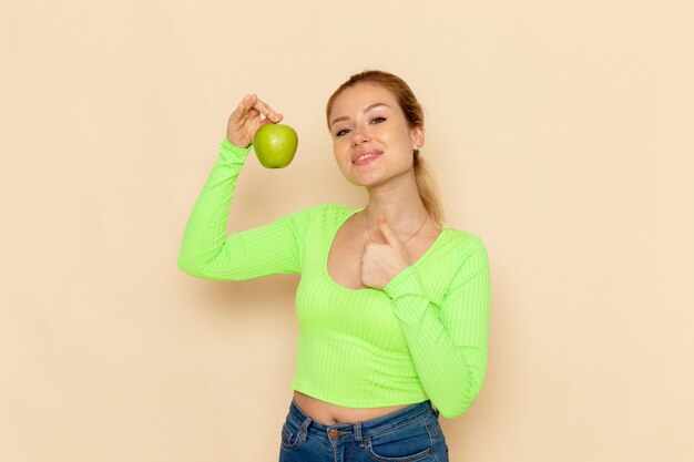 Vista frontal joven hermosa mujer en camisa verde con manzana verde fresca en escritorio crema frutas modelo mujer suave