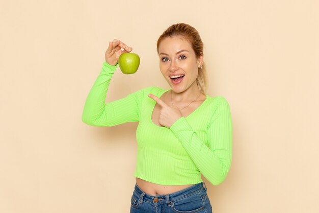 Vista frontal joven hermosa mujer en camisa verde con manzana verde fresca en pared crema modelo de fruta mujer suave