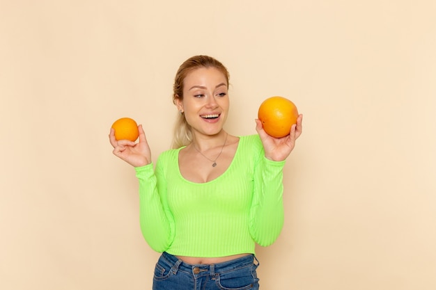 Vista frontal joven hermosa mujer en camisa verde con naranjas frescas en la pared crema modelo de fruta mujer suave