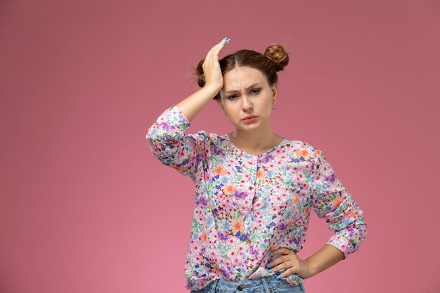 Vista frontal joven hermosa mujer en flor diseñada camisa y jeans con dolor de cabeza en el fondo rosa