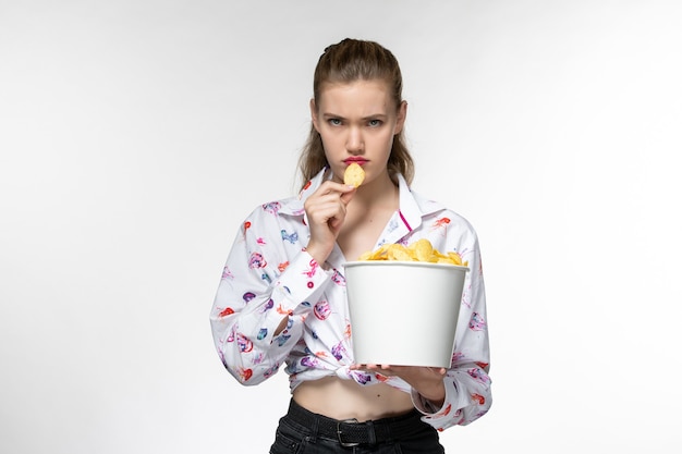 Foto gratuita vista frontal joven hermosa mujer sosteniendo cips de patata comiendo sobre superficie blanca