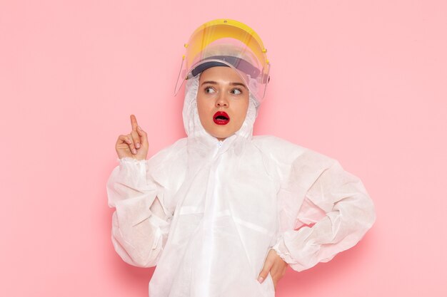 Vista frontal joven hermosa mujer en traje blanco especial con casco amarillo especial pensando en el espacio rosa traje especial niña mujer