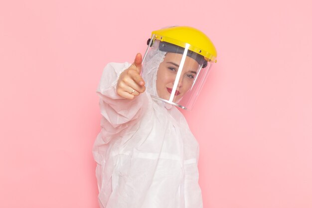 Vista frontal joven hermosa mujer en traje blanco especial con casco amarillo especial que muestra como signo en el espacio rosa traje especial niña mujer