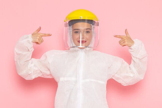 Vista frontal joven hermosa mujer en traje blanco especial con casco amarillo especial con sonrisa en el espacio rosa traje especial niña mujer