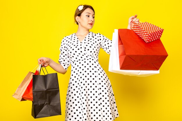 Vista frontal joven hermosa mujer en vestido de lunares blanco y negro sosteniendo paquetes de compras en amarillo