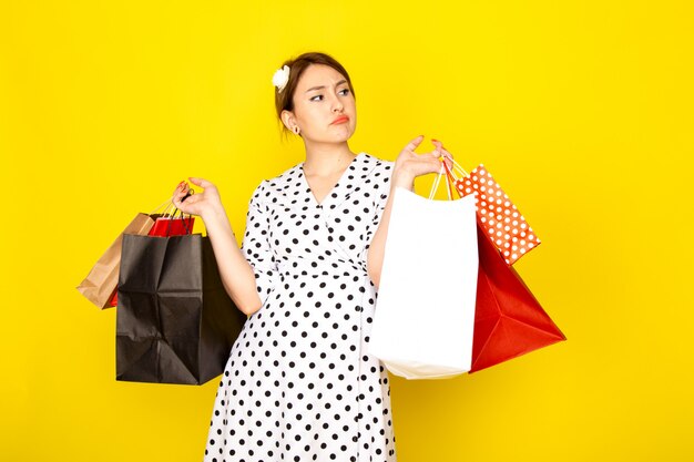 Vista frontal joven hermosa mujer en vestido de lunares blanco y negro sosteniendo paquetes de compras en amarillo