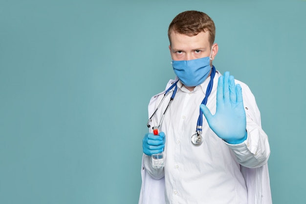 Una vista frontal joven hombre de advertencia en blanco traje médico guantes y máscara en el espacio azul