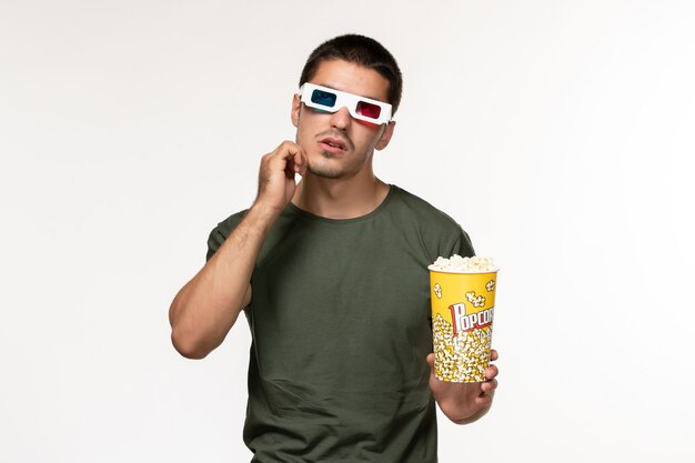 Vista frontal joven hombre en camiseta verde sosteniendo palomitas de maíz en gafas de sol d viendo la película pensando en la pared blanca película cine solitario películas masculinas