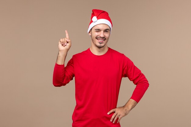 Vista frontal joven hombre guiñando un ojo y sonriendo sobre fondo marrón color masculino emoción vacaciones