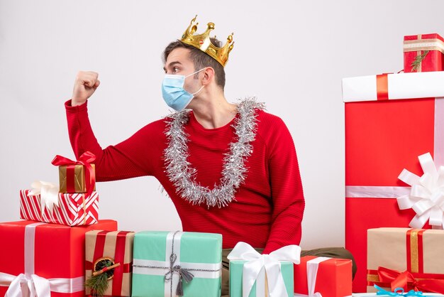 Vista frontal joven hombre de Navidad con máscara sentado en el suelo regalos de Navidad