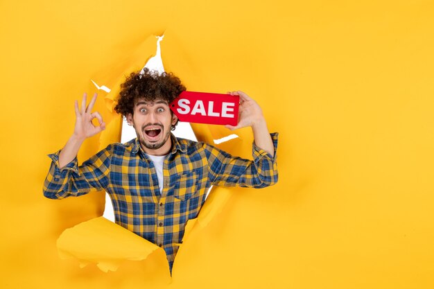 Vista frontal joven hombre sosteniendo venta rojo escrito sobre fondo amarillo rasgado