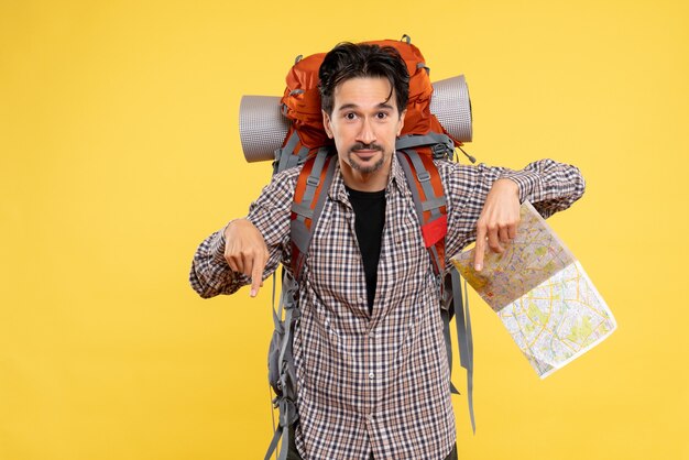 Vista frontal joven hombre yendo de excursión con mochila sosteniendo mapa sobre fondo amarillo viaje de empresa aire naturaleza campus bosque colores