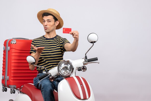 Vista frontal del joven inteligente con sombrero de paja en ciclomotor con tarjeta de descuento