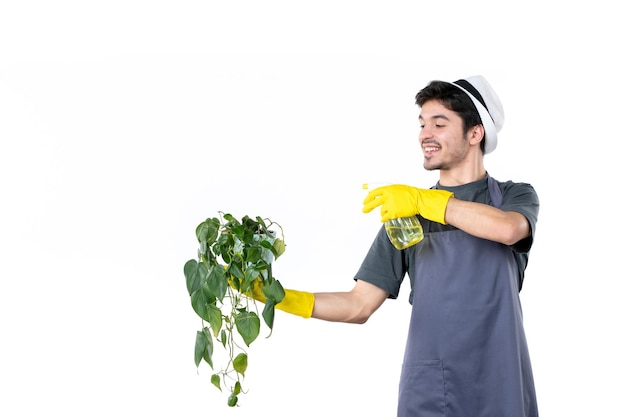 Vista frontal joven jardinero masculino sosteniendo la planta en maceta y rociando sobre fondo blanco flor trabajo árbol hierba color tierra jardín