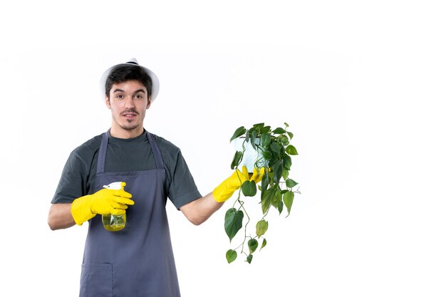 Vista frontal joven jardinero masculino sosteniendo la planta en maceta y rociando sobre fondo blanco flor trabajo árbol hierba color trabajo jardín