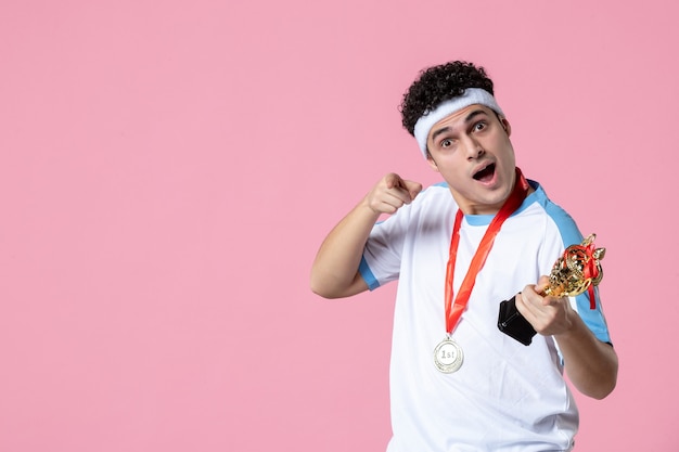 Vista frontal joven jugador en ropa deportiva con copa de oro y medalla en pared rosa claro