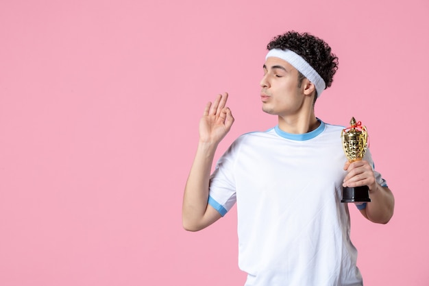 Vista frontal joven jugador en ropa deportiva con copa de oro en pared rosa