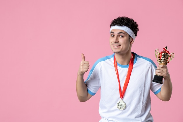 Vista frontal joven jugador en ropa deportiva con copa de oro en pared rosa