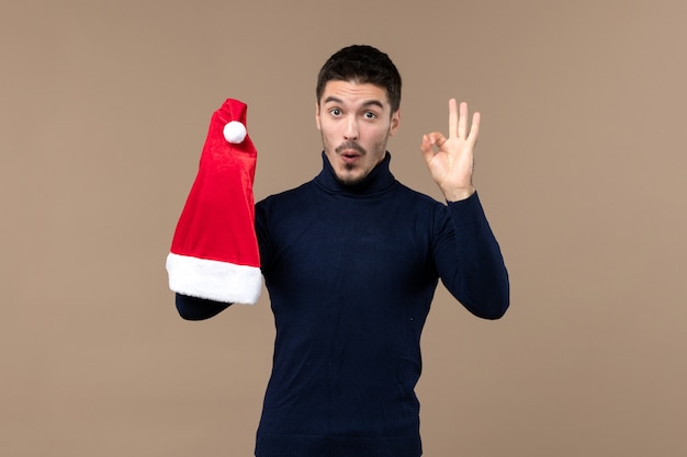 Vista frontal joven jugando con gorra roja en un escritorio marrón emociones navidad año nuevo