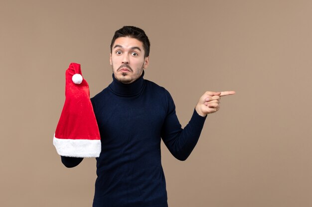 Vista frontal joven jugando con gorra roja sobre fondo marrón emoción navidad año nuevo