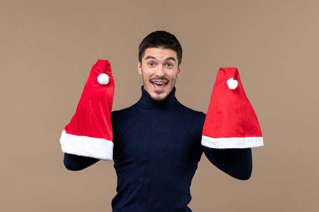 Vista frontal joven jugando con gorras rojas sobre fondo marrón emociones navideñas año nuevo