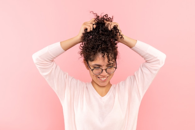 Vista frontal de la joven jugando con su cabello en la pared rosa